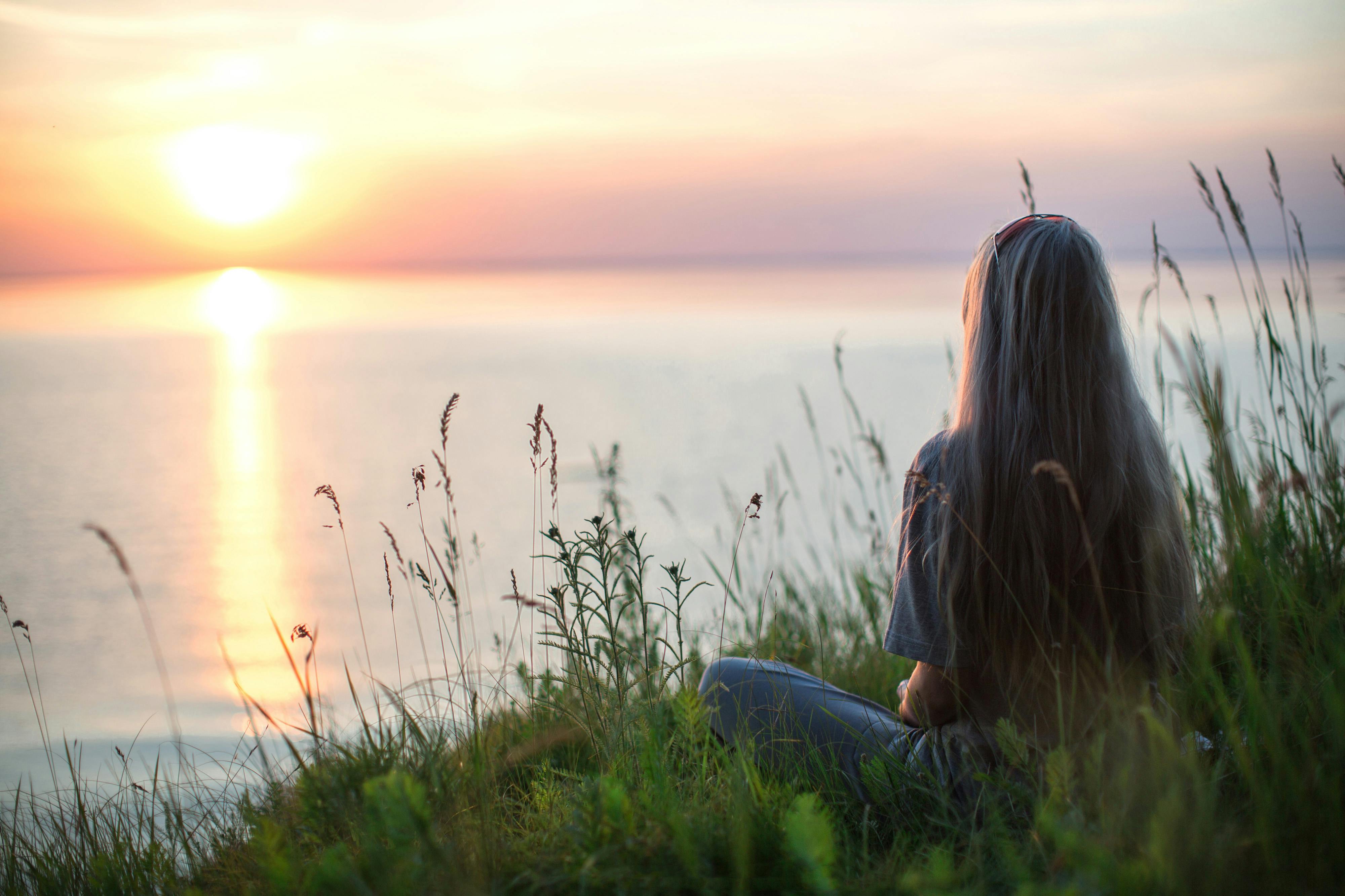 Femme assise face à la mer au coucher du soleil